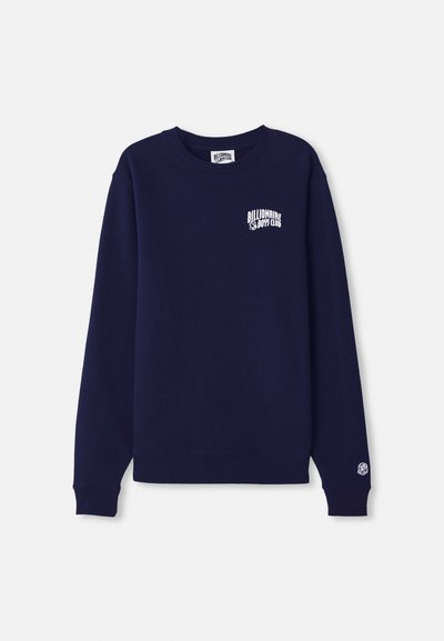 Mørkeblå crewneck genser laget av bomull med en liten hvit logo på brystet og et logomerke på mansjetten. Klassisk passform, ribbestrikket kant.
