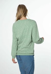 Sweat-shirt vert à motifs de pois blancs, texture douce, col rond, poignets et ourlet côtelés; porté avec un pantalon en denim bleu.