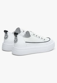 Białe sneakersy z gładką skórzaną cholewką, grubą gumową podeszwą, czarnymi akcentami na pięcie oraz naszywką z logo z tyłu. Niski design.