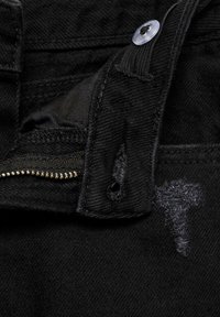 Pantalons en denim noir avec fermeture éclair et bouton. Textures usées notables et détails de couture près de la zone de fermeture.