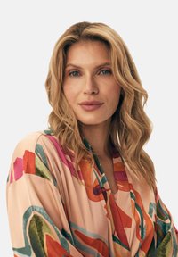 Zwiewny, kwiatowy kimono w jasnoróżowym materiale, z odważnymi akcentami akwareli w kolorze czerwonym, zielonym i niebieskim. Lekka i miękka tekstura.