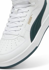 Białe trampki wykonane z leather, z zielonym paskiem Puma, złotym logo, perforowaną czubkiem i białymi sznurówkami. Okrągła podeszwa z detalicznym stębnowaniem.