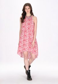 Rochie roșie și albă cu un model floral, cu decolteu halter și un tiv asimetric. Purtată cu cizme negre cu șiret.