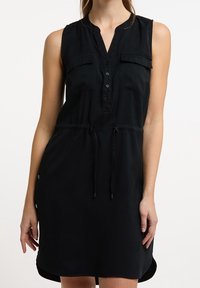 Vestido negro sin mangas con cuello tipo camisa, lista de botones, dos bolsillos en el pecho y cintura ajustable con cordón, presentando una textura suave.
