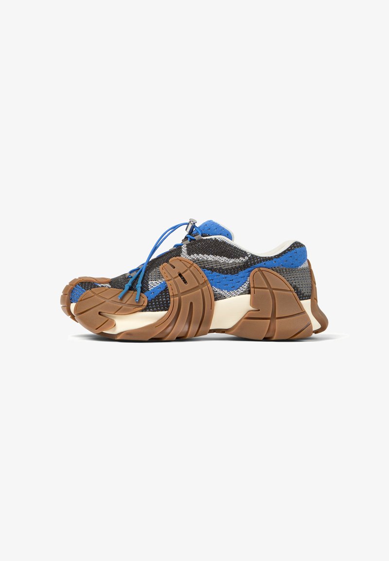 Zapatilla deportiva de corte bajo con empeine de punto en azul, negro y gris, suela segmentada marrón y cordón elástico azul con cierre de seguro.