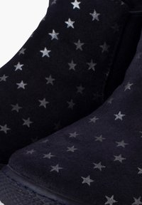 Botines de ante negro con patrones de estrellas plateadas, puntera redondeada y lados texturizados con paneles elásticos para un fácil calce.
