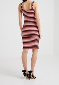 Gestreiftes Midikleid mit Rüschenträgern, das abwechselnd rote und schwarze Streifen zeigt. Figurbetonte Silhouette und gewellter Saum. Schwarze High-Heels.