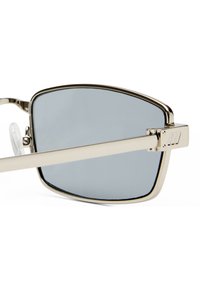 Ochelari de soare metalici cu lentile gri dreptunghiulare, un cadru subțire din argint și pernițe pentru nas reglabile din plastic transparent. Prezintă accente distinctive cu dungi pe brațe.