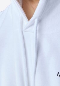 Hoodie bianco con tasca a marsupio, cordini e polsini a costine. Presenta un semplice testo nero sulla parte anteriore. Realizzato in morbido materiale in cotone misto.