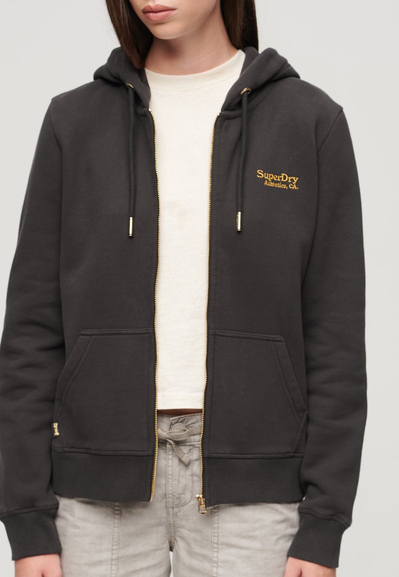 Dunkelgraue Zip-Hoodie aus Baumwolle mit goldenen Beschlägen, doppelten Fronttaschen und gesticktem Logo auf der Brust. Glatte Textur.