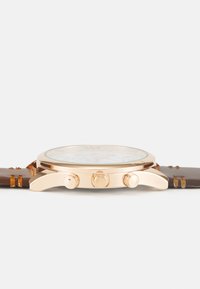 Reloj cronógrafo con caja de acero inoxidable en tono dorado, correa de cuero marrón, esfera blanca con marcadores y tres subesferas.