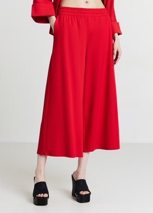 Pantaloni rossi stile culotte con vita elastica, dotati di tasche laterali e texture liscia, abbinati a sandali platform neri.