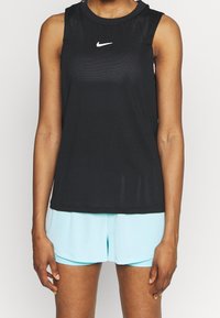 Top atlético sin mangas de color negro con tejido de malla texturizado, que presenta un logo blanco de Nike en el pecho. Combinado con pantalones cortos de color azul claro.