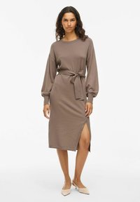 Robe longue marron à manches longues avec taille ceinturée et fente latérale. Tissu lisse avec une coupe décontractée, présentant des poignets côtelés et un col rond.