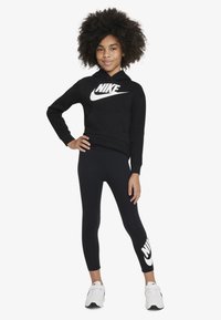 Black Nike hoodie with a large white logo, paired with black leggings featuring a white logo on one leg, worn with white sneakers.
