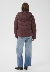 Mørkerød pufferjakke med hætte, der har et chevron-quiltet mønster. Parret med lyseblå brede bukser og sorte hælede støvler.