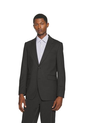 Czarna marynarka z klapami typu notch, zapięcie na jeden guzik, dwie przednie kieszenie oraz pasujące spodnie. Połączona z jasnoniebieską koszulą w paski.