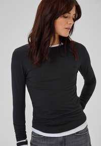 Juodas ilgas rankovės marškinėliai su slim fit siluetu. Savinasi baltas apvalus iškirpimas ir kontrastingas baltas apdaila. Lygi tekstūra, pagaminta iš tampančios medžiagos.