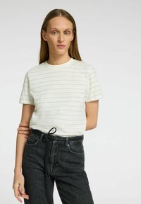 Vit kortärmad t-shirt med ljusblå horisontella ränder. Mjuk tyg, rundad halsringning, kombinerad med mörka högmidjade jeans med bälte.
