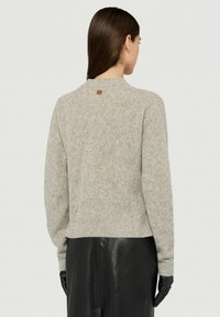 Szary sweter w wzór w jodełkę z okrągłym dekoltem, prążkowanymi mankietami i dołem. Posiada małą brązową metkę z tyłu przy dekolcie.