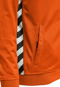 Pomarańczowy sweatshirt z fakturowanej tkaniny, boczną kieszenią oraz kontrastowym czarno-białym panelem w paski z perforowanymi detalami.