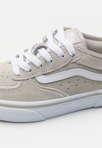 Tan suede sneakers with white laces, perforated design, and white side stripes. Features padded collar and rubber sole.