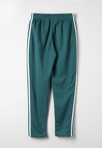 Pantaloni sweats verde teal con vita elasticizzata e strisce bianche laterali, distesi su uno sfondo grigio chiaro.