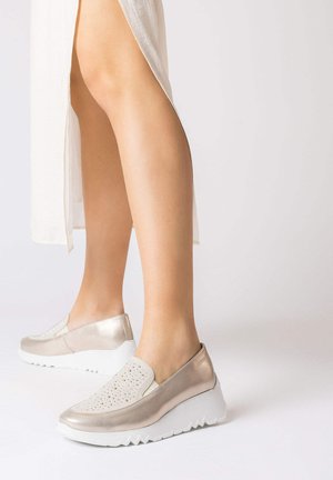 Chaussures slip-on dorées métalliques avec panneaux latéraux perforés et semelles en caoutchouc blanches. Design compensé surélevé avec surface texturée.