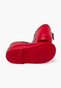 Zapatos rojos de goma con punta redondeada, suela plana y pequeño detalle de hebilla en el costado. Suela texturizada para mayor agarre. Acabado suave.