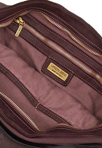 Interno di una borsa in pelle bordeaux con molte tasche con zip, foderato in tessuto e un'etichetta dorata che recita "Caterina Lucchi Made in Italy."