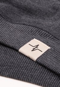 Beanie grigio lavorato a maglia con risvolto, caratterizzato da un motivo testurizzato. Un'etichetta rettangolare crema con logo nero è attaccata al risvolto.