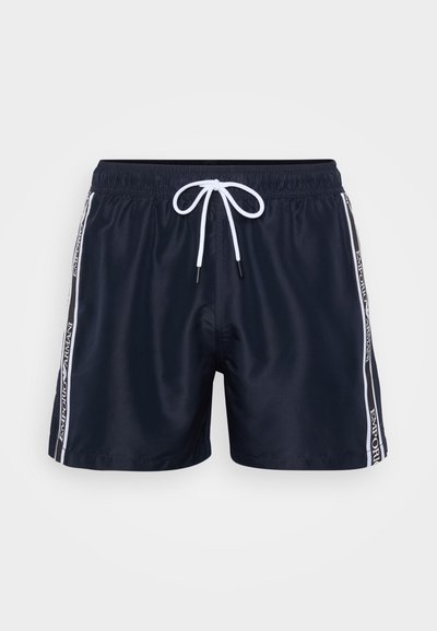Navy swim shorts featuring an elastic waistband with white drawstring, side stripes with logo detailing, and a smooth, lightweight fabric.