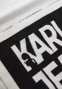 Fekete-fehér pamut anyag, amelyen merész fekete betűk és grafikus részlet található, texturált felszínnel és kontrasztos varrásokkal.
