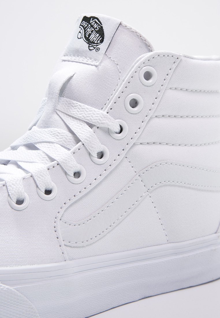 Zapatillas altas de lona blanca con cordones redondos, ojales de metal y suela de goma. Presentan detalles de costura y una etiqueta de marca en la parte superior.