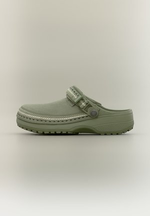 Groene instapklomp met verstelbare riem, gestructureerde zool en decoratieve witte stiksels aan de bovenzijde.