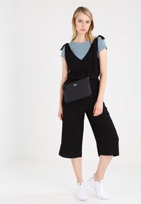 Completo nero con pantaloni cropped, design a scollo a V, abbinato a una maglietta azzurro chiaro. Indossato con sneakers bianche e una piccola borsa a tracolla nera.