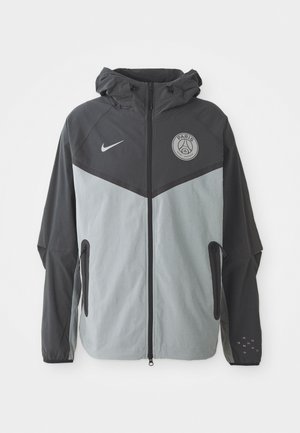 Jachetă Nike Paris Saint-Germain cu glugă, având un sistem de culori negru și gri deschis, cu fermoar frontal și logo pe piept.