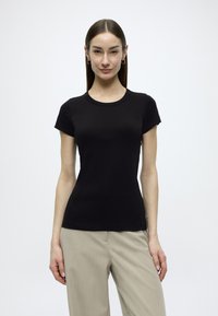 Μαύρο t-shirt με κοντά μανίκια από μαλακό ύφασμα, με στρογγυλή λαιμόκοψη και εφαρμοστή γραμμή. Χωρίς σχέδια ή εμφανή εξαρτήματα.