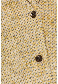 Manteau en laine présentant un motif texturé jaune et bleu, avec un bouton sombre comme détail de fermeture. Le tissu est tissé dans un style lâche et confortable.