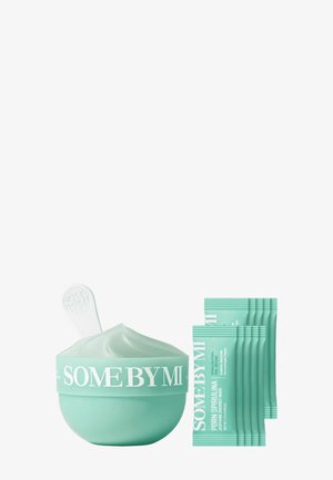 Pot vert menthe de crème de masque en tissu apaisant Some By Mi Pore Spirulina avec plusieurs sachets et une petite spatule sur fond blanc.