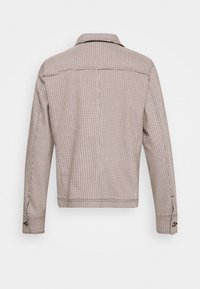 Veste en tissu pied-de-poule beige et marron montrée de dos, avec des manches longues, des poignets boutonnés et un ourlet droit.