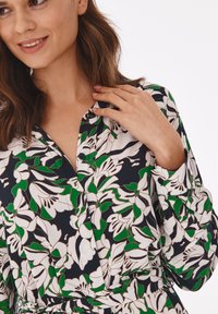 Bluse mit floralem Muster auf navy Hintergrund, mit weißen und grünen Blumen, Knopfdetails und klassischem Kragen.