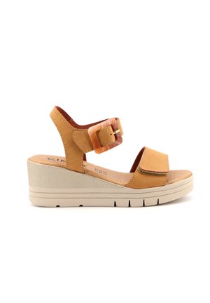 Sandalo con zeppa color cuoio con cinturino regolabile alla caviglia, grande fibbia quadrata e ampia fascia frontale sopra le dita dei piedi.