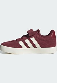 Burgundijska suknjasta cipela s bijelim trakama i čičak trakama. Sadrži ravni, teksturirani potplat i dizajn s okruglim vrhom.