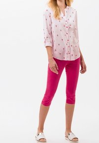 Camisa blanca de botones con estampado de langosta rosa, mangas remangadas; pantalones cortos rosas; sandalias plateadas con tiras.