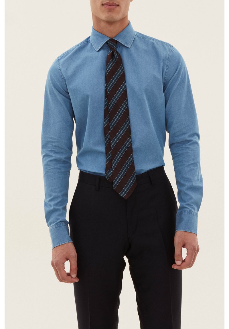 Chemise bleu clair à manches longues associée à une cravate à rayures diagonales marron et bleu, portée avec un pantalon foncé ajusté. Coupe ajustée, texture lisse.