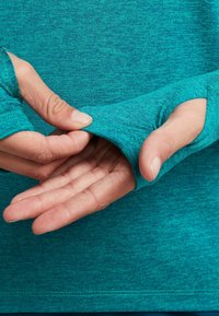 Teal long-sleeve top with thumbholes. The fabric features a textured, heathered pattern and smooth finish for comfort and flexibility.