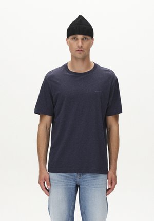 Navy blue jersey t-shirt with a round neckline and short sleeves, paired with light blue denim jeans, modeled by a person wearing a black knit beanie.
