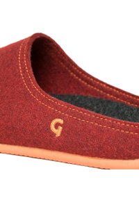 Red felt slipper with a curved opening, orange stitching, and a textured black interior. Features a small, embroidered 'G' logo.