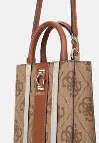 Bolso de mano marrón con un estampado, acentos de cuero sintético suave, que cuenta con dos asas en la parte superior, una correa removible y un detalle de hardware con logotipo.